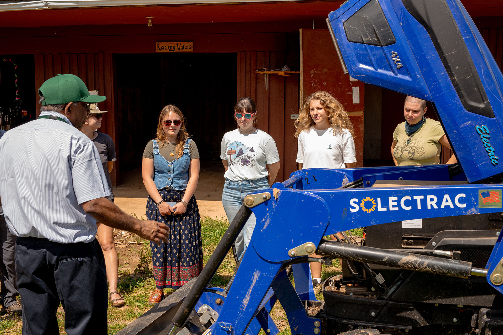 Master of Science in Applied Climate Studies students stand outside beside the Solectrac electric tractor that has its hood raised for students to examine its inner workings.