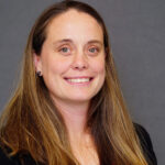 Warren Wilson College Associate Athletic Director Katie Wurst stands smiling in front of a grey background.