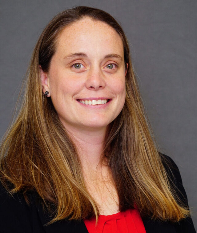 Warren Wilson College Associate Athletic Director Katie Wurst stands smiling in front of a grey background.