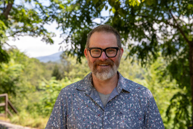 Sustainable Agriculture professor Tony VanWinkle stands and smiles in front of a backdrop of the mountains
