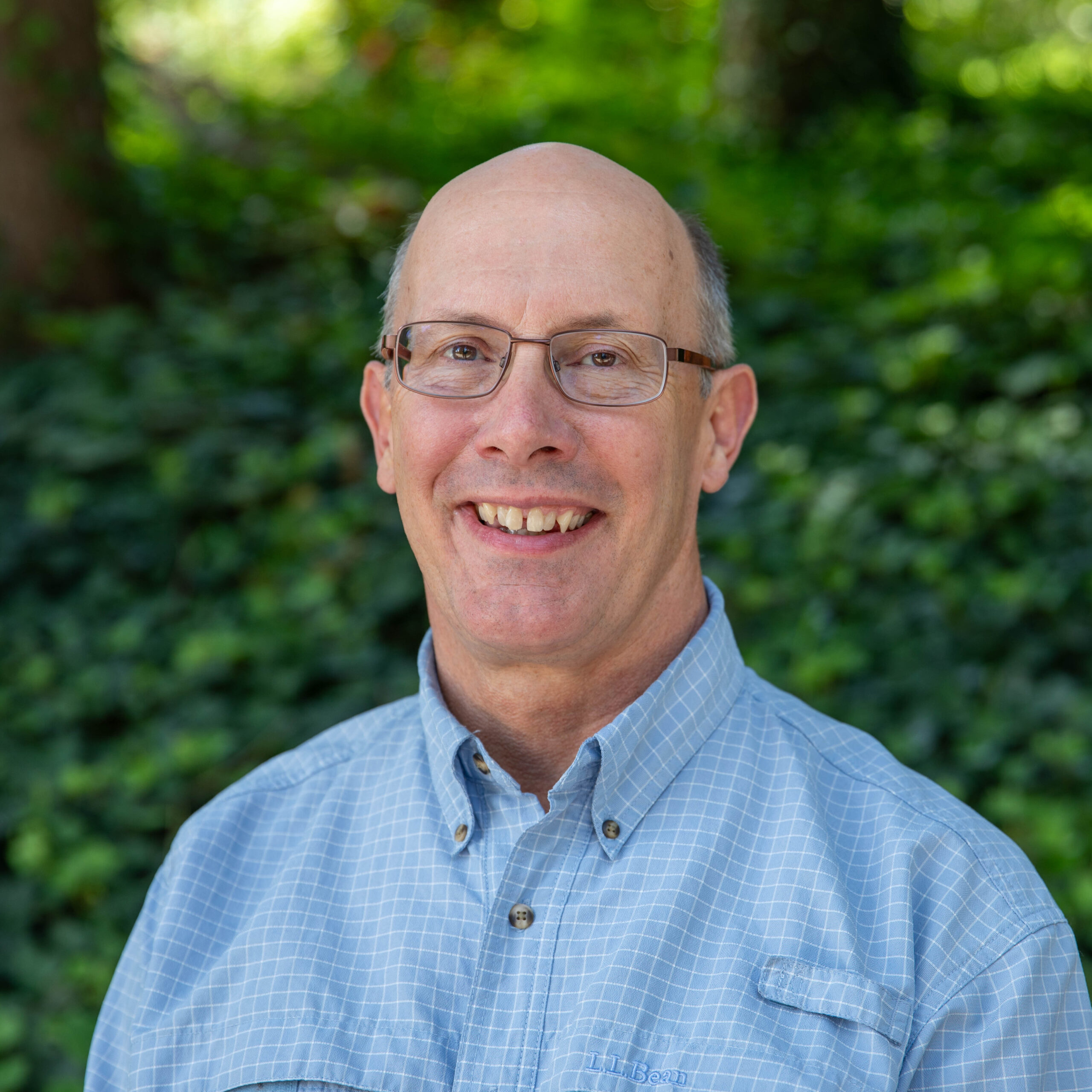 Executive Director of Operations Ian Smith stands smiling in front of a forest background.