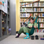 Embracing Neurocomplexity: A student sits in a hammock chair in the library studying on their laptop.