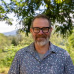 Sustainable Agriculture professor Tony VanWinkle stands and smiles in front of a backdrop of the mountains