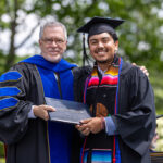A student smiles with the president of the college at commencement.