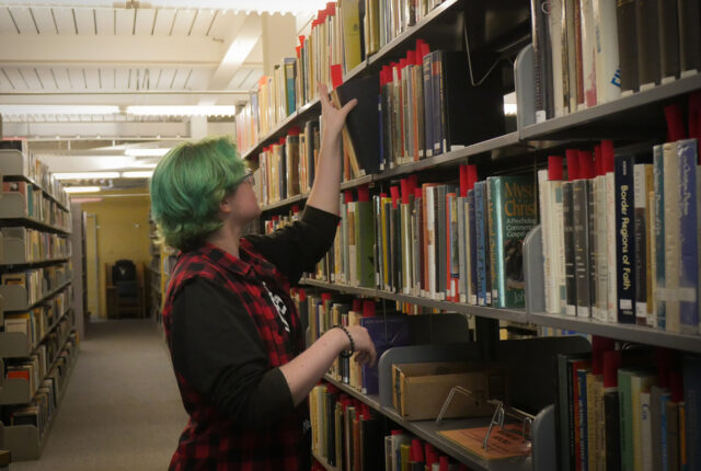 A library circulation crew student files books away.
