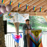 Director of the Queer Resource Center, Jo Go, speaks to those gathered at the lavender graduation. Various Pride flags are hung up in the background.