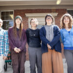 Students and Professor Christopher Potvin stand and smile in front of a building