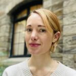 Assistant Director of the MACS program, Delilah Griswold, smiles in front of a stone wall.