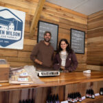 Two people stand smiling behind the counter of the Farm General Store