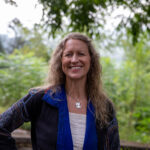 Visiting Professor Hayley Joyell stands smiling with the background of the mountains.