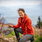 Assistant Professor of Conservation Biology, Laura Boggess, on one knee posing for a picture with the backdrop of mountains.