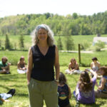 Mallory McDuff standing in a pasture with students sitting in a circle behind her.
