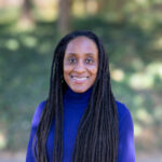 Dr. Delicia Daniels, creative writing professor, stands smiling in front of a natural background