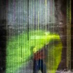 Professor Kathryn Cellerini Moore poses at an exhibition behind metal chains that hang from the ceiling. A bright green and yellow spotlight shines towards them.