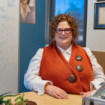 Dr. Lucy Lawrence sits at a table in her office and smiles at the camera.