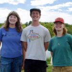 Three Warren Wilson College Students stand smiling at their fellowship in tennessee at Caney Fork Farms